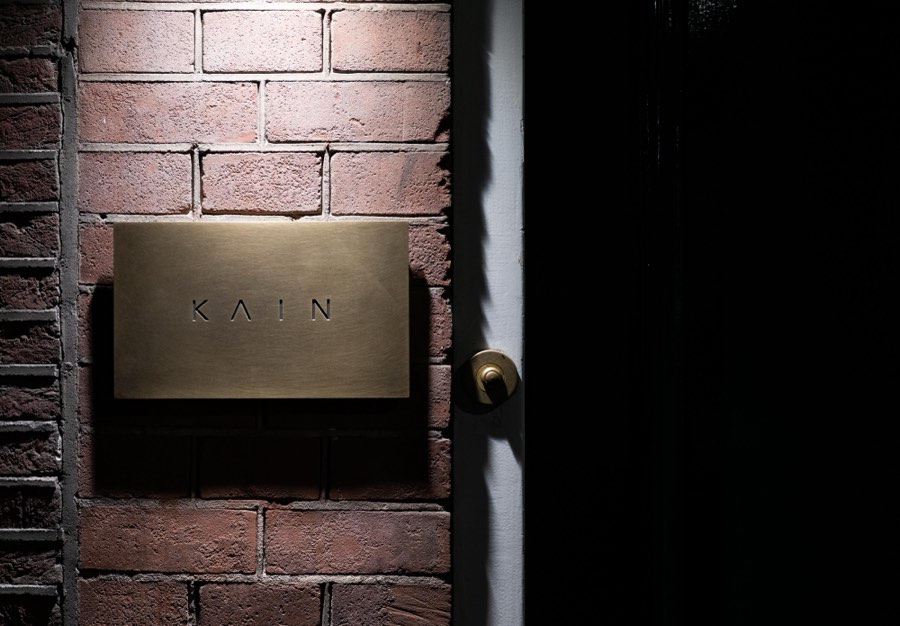 Brass KΛIN sign on the brick wall beside the entrance
