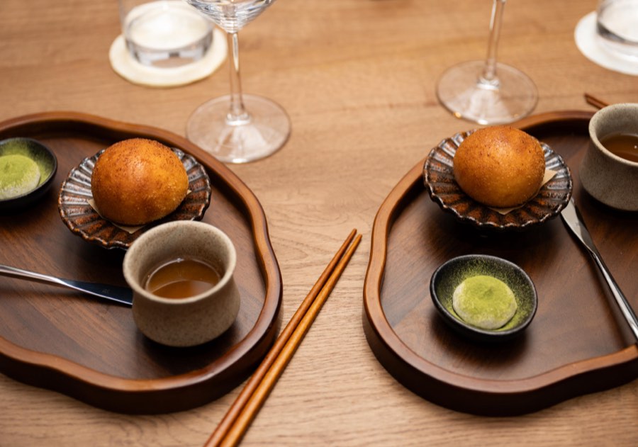 Two golden fried dishes served on wooden trays with broth and matcha-dusted mochi