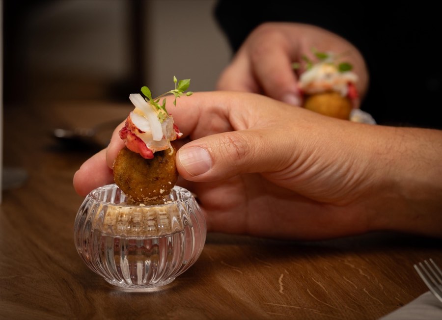 A hand lifting a crisp bite topped with langoustine and fresh herbs
