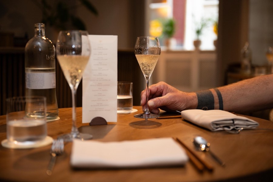 A table set with sparkling wine, the menu and a guest's hand on a glass